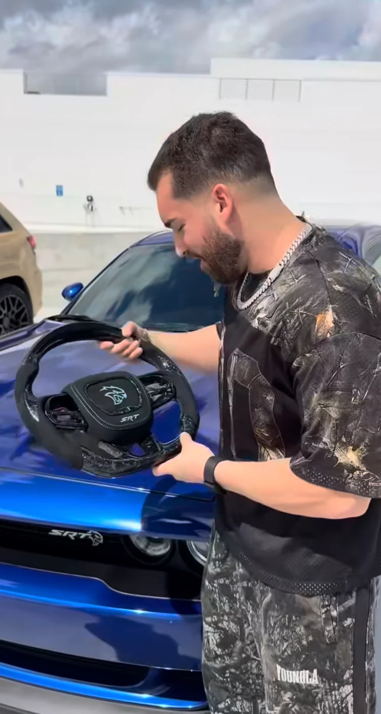 Carbon Hellcat steering wheel held over a blue Dodge Challenger