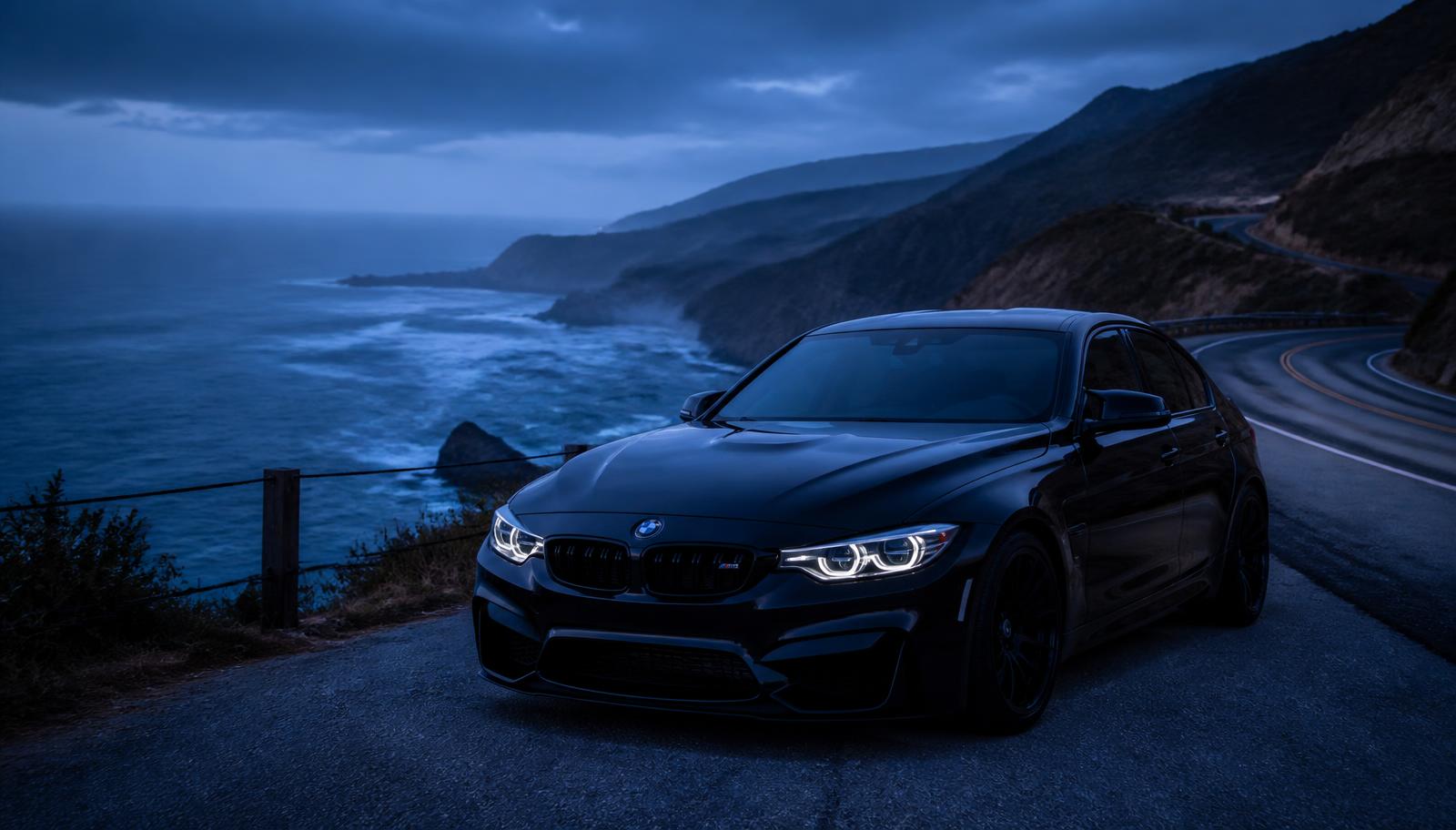 Blacked-out BMW M on a coastal cliff road at blue hour