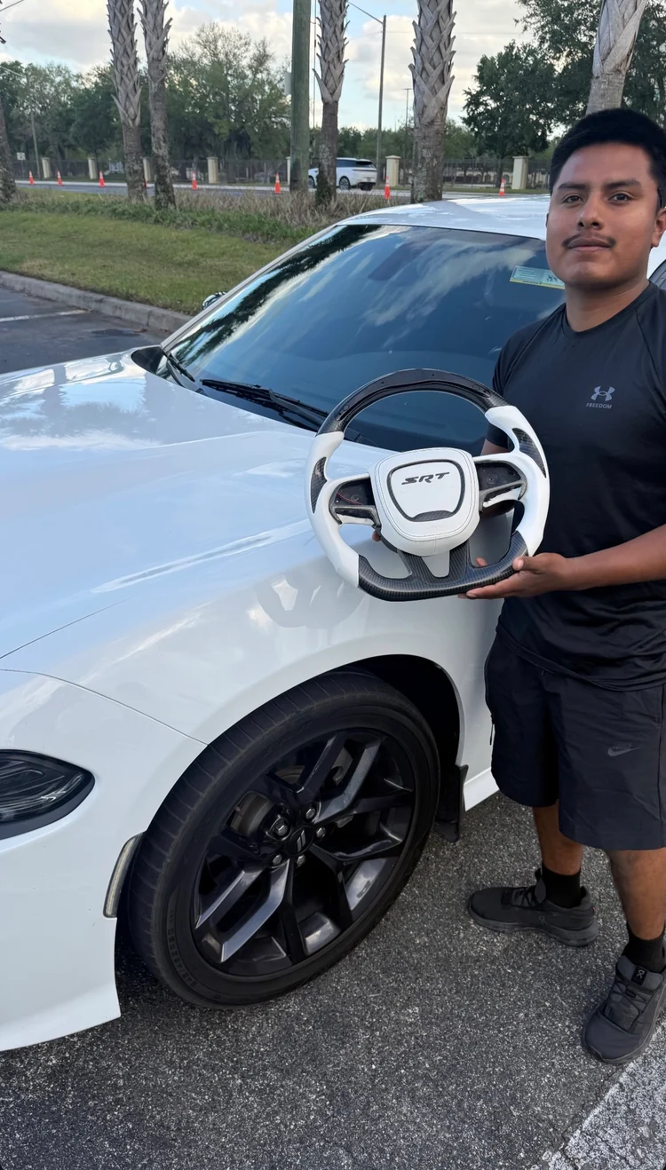 White and carbon SRT steering wheel held beside a white Dodge Charger